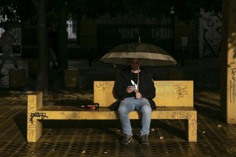 ep joven sentado en un banco bajo su paraguas