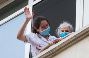 ep una sanitaria ayuda a una paciente mayor a salir a la ventana para rendir homenaje a los
