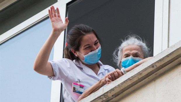 ep una sanitaria ayuda a una paciente mayor a salir a la ventana para rendir homenaje a los