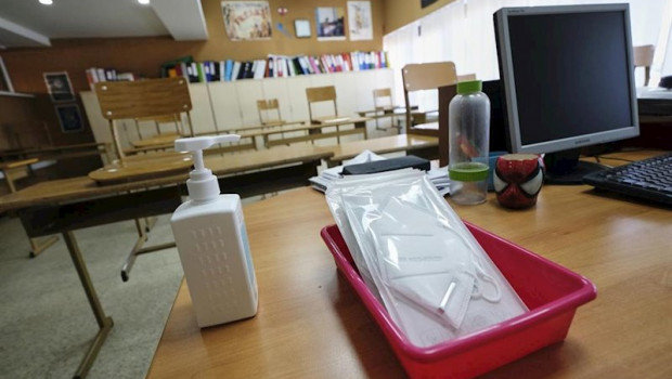 ep mascarillas y gel desinfectante en la mesa del profesor de un aula donde se pueden observar los