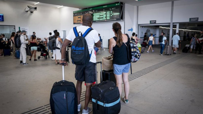ep varias personas esperan con maletas y observan los carteles de salidas en la estacion de