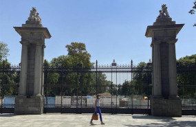 ep una mujer pasa al lado de una de las puertas del parque de el retiro