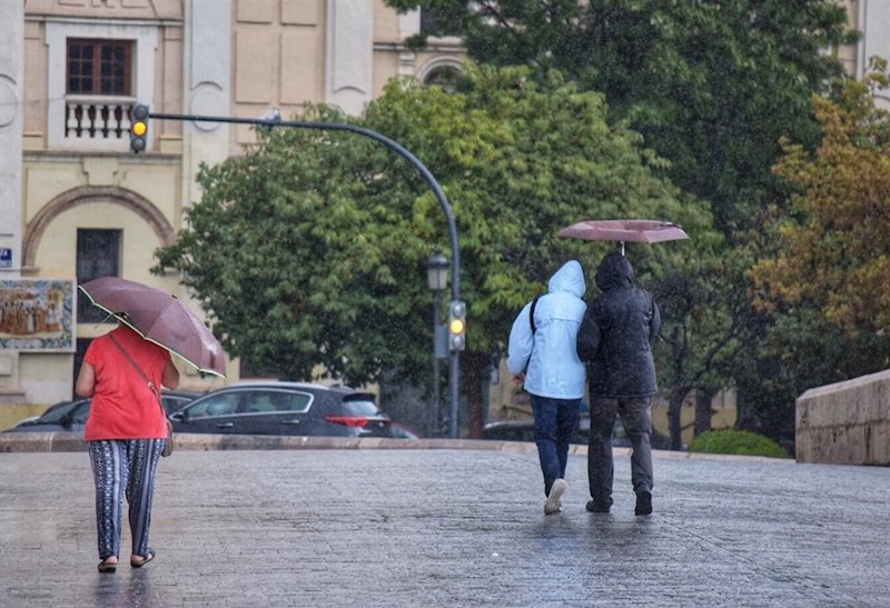 ep varias personas pasean por una calle de valencia con paraguas y chubasqueros