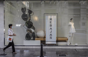 ep una mujer protegida con mascarilla pasa al lado del escaparate de una tienda donde se observan